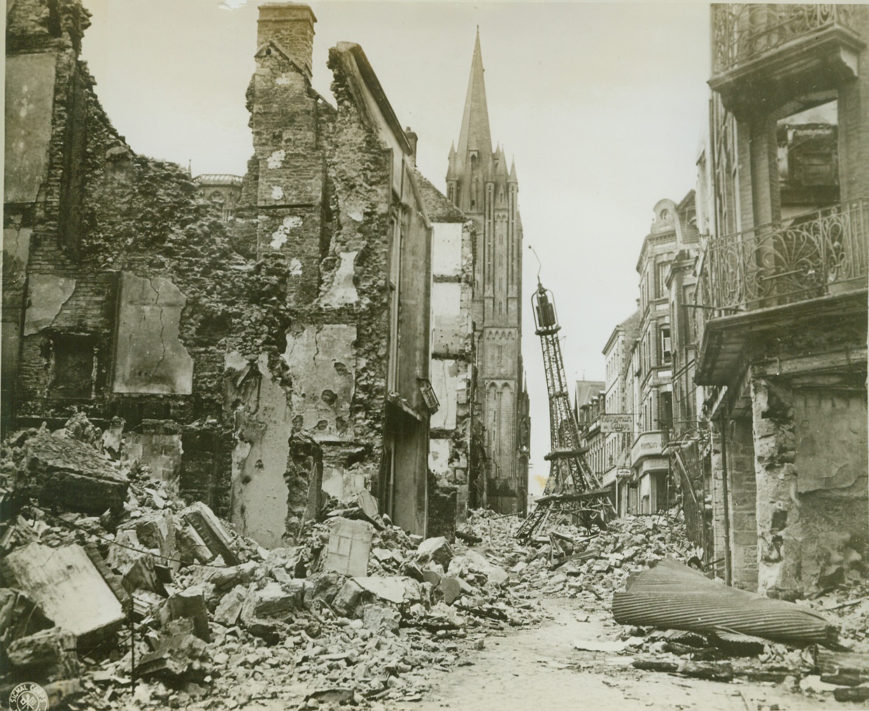 Miniature Eiffel Tower Amid Wreckage, 8/3/1944. France—Flanked by war-torn buildings, a small replica of the famous Eiffel Tower rests atop a heap of rubble in a Coutances Street. In the center, background, is the Cathedral, seemingly undamanged. Credit: U.S. Army photo from ACME;