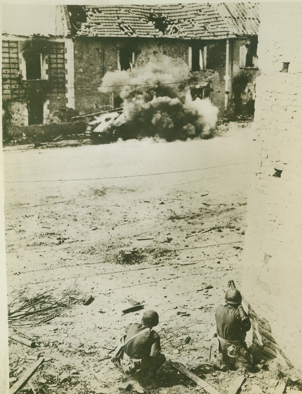 Removing German Tank Obstacle, 8/1/1944. Normandy, France—The camera records the instant when the bazooka guns fired by the Allied soldiers in the foreground score direct hits on the German tank in the rear, and the vehicle goes up in a cloud of flame and smoke. The soldiers were aiming at the wrecked building which housed German snipers, but the tank was blocking their attack. Credit: ACME;