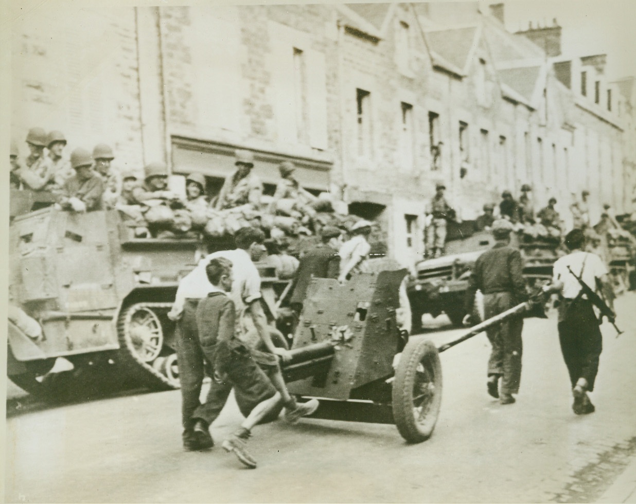 Frenchmen Retrieve German Gun, 8/4/1944. France—As American and Allied forces watch from trucks at the side of the road, civilians of Brehal, France, bring in German equipment left behind by the rapidly retreating Nazis. Little boy rides the barrel of a light infantry cannon being rolled through the town. Credit: Signal Corps radiotelephoto from ACME;