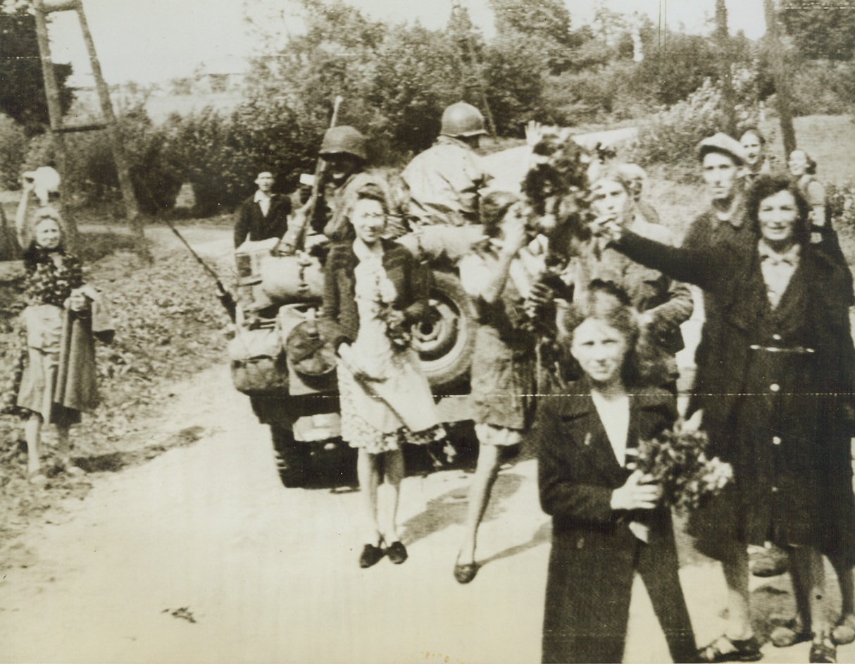 Flowers for the Liberators, 9/4/1944. FORGE PHILLIPPE, BELGIUM—Women and children of Forge Phillippe carry bouquets of flowers to throw in the path of the American Liberators of their town. They crowd about two Yanks in a jeep as the little vehicle rolls through the village. Credit: ACME PHOTO VIA ARMY RADIOTELEPHOTO.;