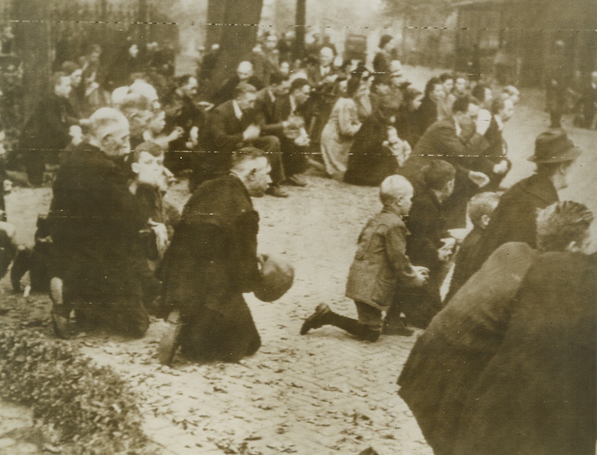 HOLLANDERS PRAY FOR NAZI VICTIMS, 9/26/1944. Bareheaded villagers of Leende, Holland, kneel in prayer in the streets of the city, in tribute to the memory of four of their number killed by the Nazis as the latter retreated from Leende. Credit: British official photo via U.S. Army radiotelephoto from Acme;
