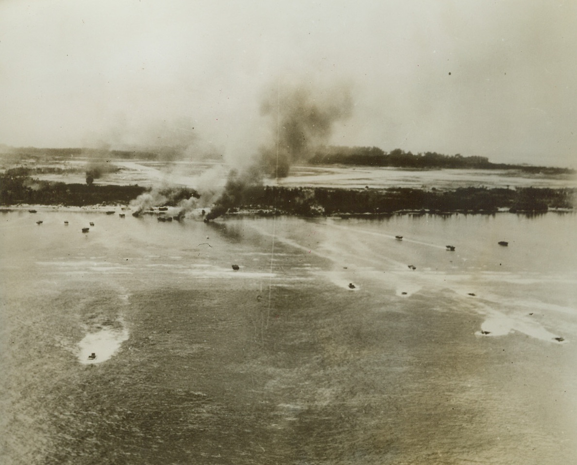 Fight for Peleliu, 9/22/1944. Peleliu Island, Palau – Looking like water bugs, Marine “Amtracks” dart through the shore waters of Peleliu Island as a Naval Barrage is laid down to cover the invasion. Several of the amphibious tractors, targets of Jap mortars, burn near the beach. The Jap airfield, prime objective on the island, can be seen beyond the fringe of trees. Credit: Official U.S. Navy photo from ACME;