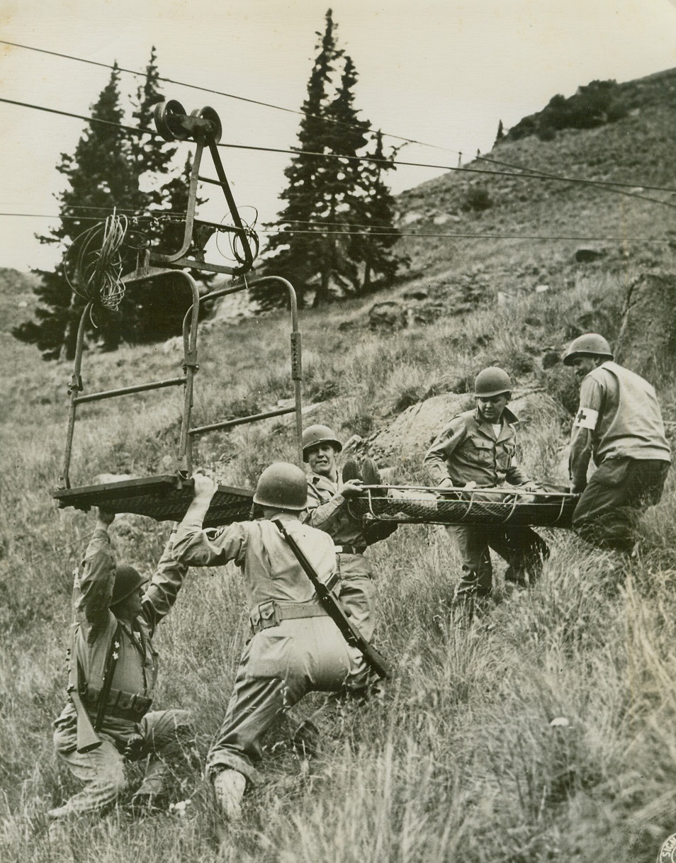 Light Aerial Tramway M-2 (1), 9/21/1944. Camp Hale, Col. – The transportation of ammunition, food, and water, the evacuation of wounded personnel, and the moving forward of artillery for mountain troops in terrain too rough for pack animals or men has long been a serious problem for mountain fighters. The Army recently offered to the public its solution of this problem here when the Camp Hale test branch of the Mountain and Winter Warfare section of the Army’s Engineer Board gave a demonstration of the recently perfected Light Aerial Tramway M-2. Near the upper Terminal of the M-2, Medical Corpsmen are shown loading a Stokes litter and simulated casualty on to the cable car. Three thousand feet below, the ambulance waits to rush the “wounded” man to a base hospital 9/21/44 Credit Line (Signal Corps Photo From ACME);