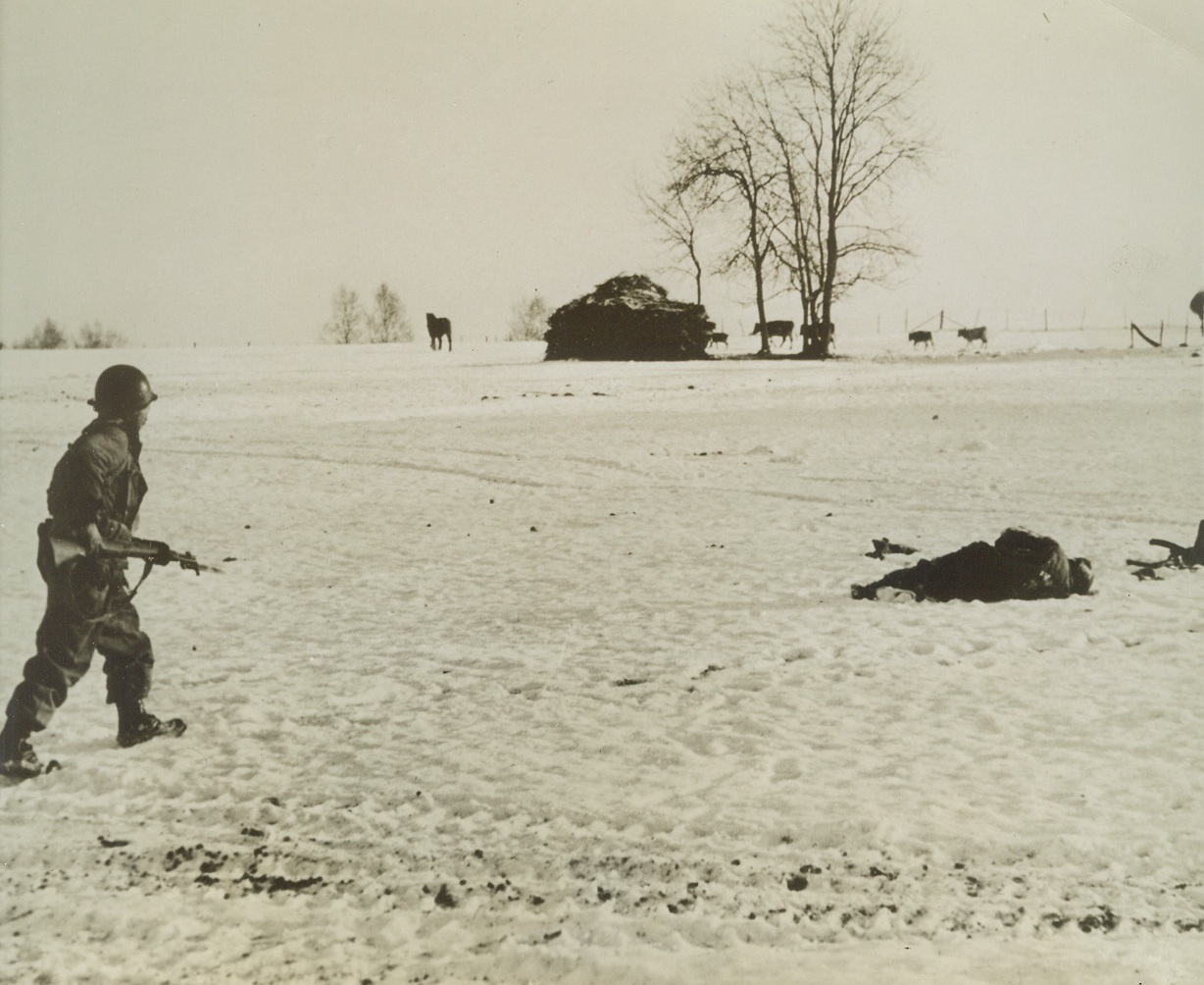 MAN IN THE SNOW, 1/6/1945. BASTOGNE, BELGIUM—Advancing cautiously across a snow-covered field, an American soldier nears the spot where a Nazi fighter lies. He keeps his gun ready for use at a moment’s notice until he finds out whether the man is dead or alive. Credit: Acme;
