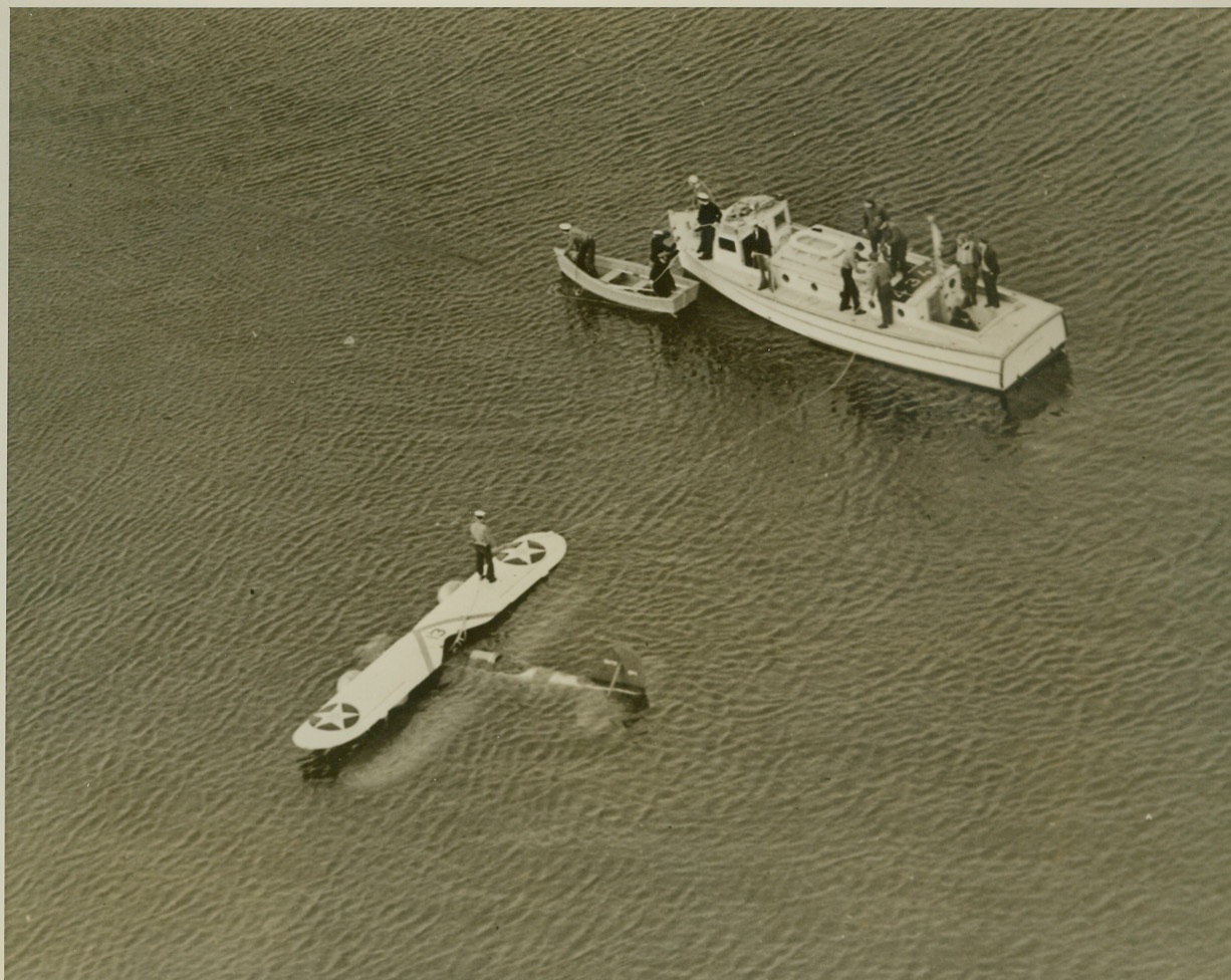 Navy Flier Sits Down Land Plane in Bay, 12/10/1940  New York—About to land his Grumman training plane at Floyd Bennett Field, Ensign Robert Winston discovered that a wheel was locked and could not be released. After dropping a note to field officials explaining his predicament, Winston sat the plane down on the waters of Jamaica Bay between two amphibians waiting for him, and climbed out with his companion, E.J. Marrone, Assistant Machinist’s Mate, nothing wet but their feet. Winston, a former test pilot, saw wartime service in France and Finland. Photo shows the plane on the bay after the occupants- with life preservers in rear of launch- had been rescued. Credit: ACME;