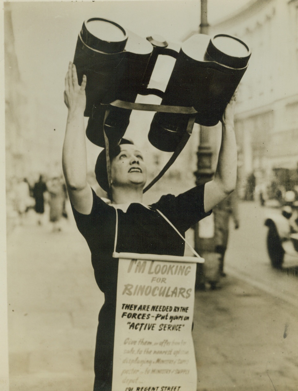 Attractive, 2/5/41  London – Attention compelling is this pretty young lady and her oversized “binoculars” as she parades through Regent Street, keeping a sharp lookout for anyone answering her appeal for binoculars for use by the fighting forces. Credit: (ACME);