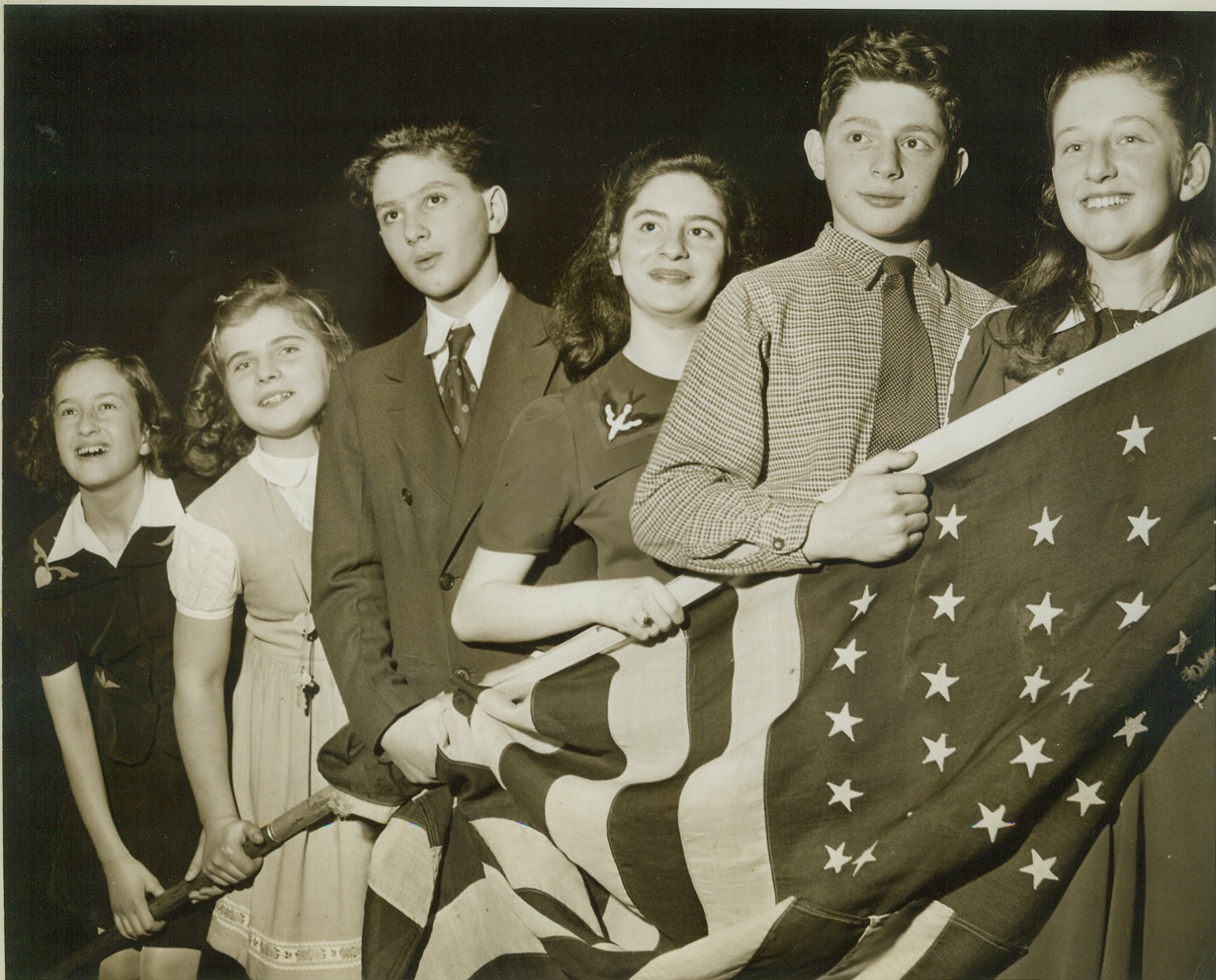 YOUNG JEWISH REFUGEE CHILDREN, 2/22/1943. NEW YORK CITY – A group of refugee children recently arrived in this country from Europe stand behind the American Flag at a Solemn Assembly of Prayer and Protest held today at the Mecca Temple by three thousand Jewish children from 518 religious schools in greater New York for the children in Nazi-occupied countries. Left to Right: Ingeborg Jacob, Germany; Ruth Friedberg, Poland; Abraham Brumberg, Poland; Helen Springer Germany; Manfred Kochen, Luxembourg; and Janine Putter, France. Credit: ACME;