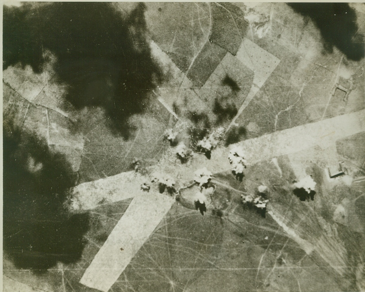 R.A.F. BLASTS JAP LANDING FIELD, 2/19/1943. BURMA- Eighteen R.A.F. bombs burst across runways on a Jap occupied airfield at Pokokku, Burma. The British bombers are hammering the Nipponese and their military installations regularly in this battle area. Most of the bursts are on runway intersections; two are on aircraft shelters. The black patches are cloud shadows. Credit: ACME;