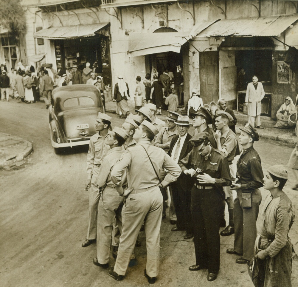 No Title, 2/2/1943. Recently the crew of a Liberator bomber of the U.S. Army Air Forces, which had been stationed in the Middle East and had seen action against the enemy, was given a short holiday. They decided to visit Jerusalem. Under the guidance of an American minister named Adams, they saw the many interesting sights in the Old and New Cities, their trip being planned for them by the YMCA. In this series of photos, which has just been released, the American fliers are shown during their visit.  NEW YORK BUREAU Members of the crew gaze up at David’s Tower as Mr. Adams (center of group) explains its history. One of the Americans gets his camera set for a picture of the scene. Credit: Acm;