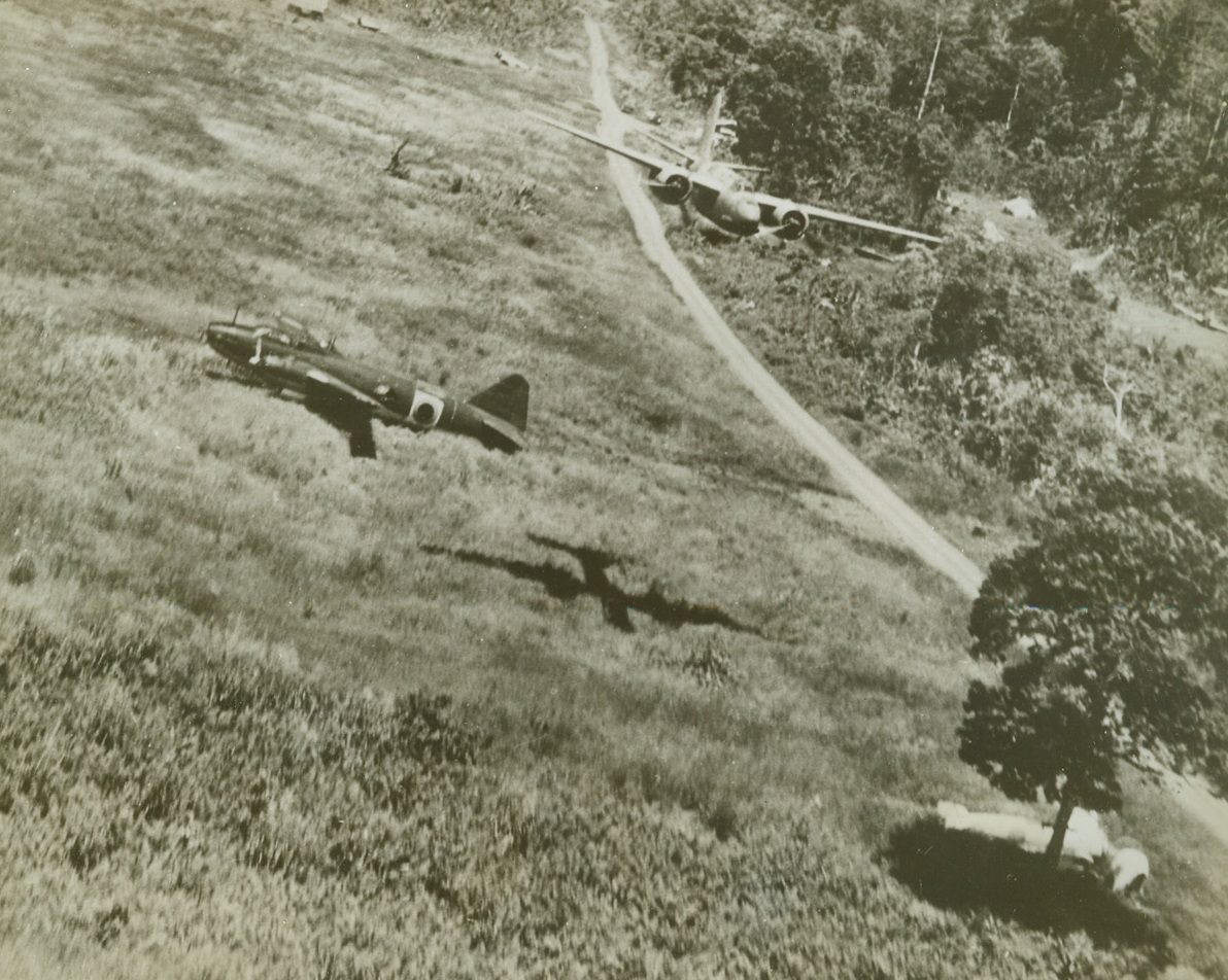 American Bomber Wallops Jap Planes, 2/2/1943. New Guinea – An American A-20 skims mere 100 feet above the ground at Lae, New Guinea, in a strafing attack on Jap planes.  It is passing over a disabled enemy bomber that will never fly again.  Under the tree (right), rests a Jap zero which has received its quota of American lead while another zero (edge of clearing, upper right) also will never see action again.  Two more enemy aircraft are near house (top center).Credit (U.S. Army Air Corps photo – ACME);