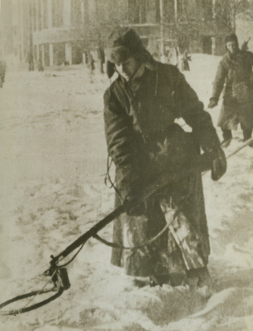 Wary Street Cleaner, 2/19/1943. Voronezh, Russia – A Russian Sapper proceeds cautiously along a street in Voronezh, hunting for Nazi mines buried beneath the snow in the industrial center recaptured by the Reds. Land mines represent a ticklish proposition for the sappers when there is a heavy snow. This one holds his detecting device far from his person. Credit: ACME;