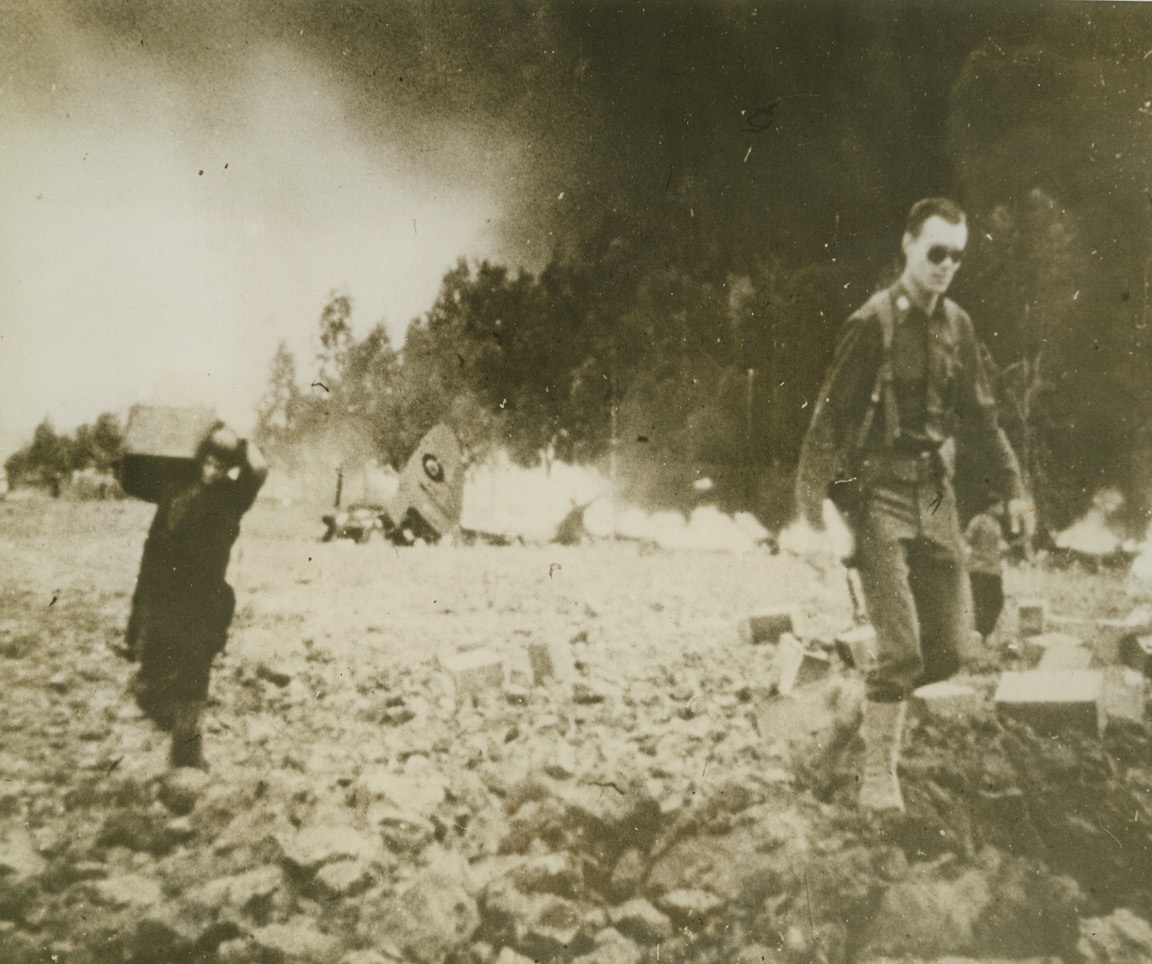 Nazis Blast Allied Air Base, 2/16/1943. Souk El Arba – Allied soldiers rush valuable supplies from the scene of Nazi bomb hits at Souk El Arba, the air base captured by allied paratroops a few days before the attack.  An allied plane flames in the background.  As American interceptors engaged the raiders, munitions were removed from flaming areas, and wounded and shell-shocked soldiers and civilians received emergency treatment on the field of battle.  The bombs hit gas and oil supplies as well as munitions dumps at the airfield but the axis, too, lost fairly heavily.  The morning following the attack, unescorted DC-3 transports brought replacement supplies and munitions to carry on the Tunisian attack.Credit (U.S. Army Signal Corps film - - ACME);