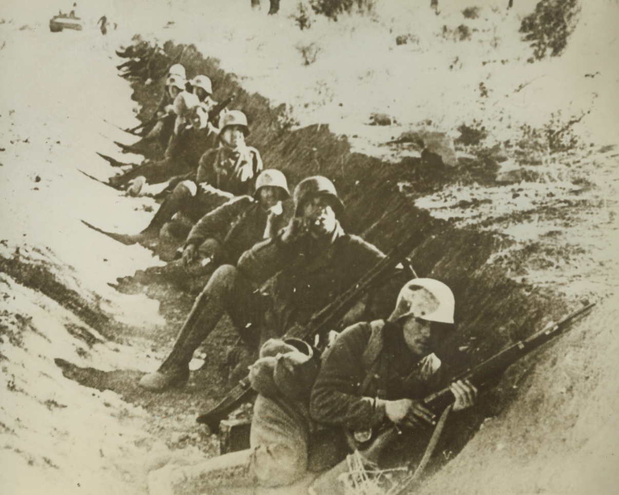 Nazi Infantry Wait in Trench, 3/1/1943. The caption of this German photo, just received in New York by way of Lisbon, says these soldiers are members of a German infantry division waiting in a shallow trench for the signal to fellow heavy tanks attacking United Nations troops “somewhere on the Tunisian front.”  Credit line (ACME);