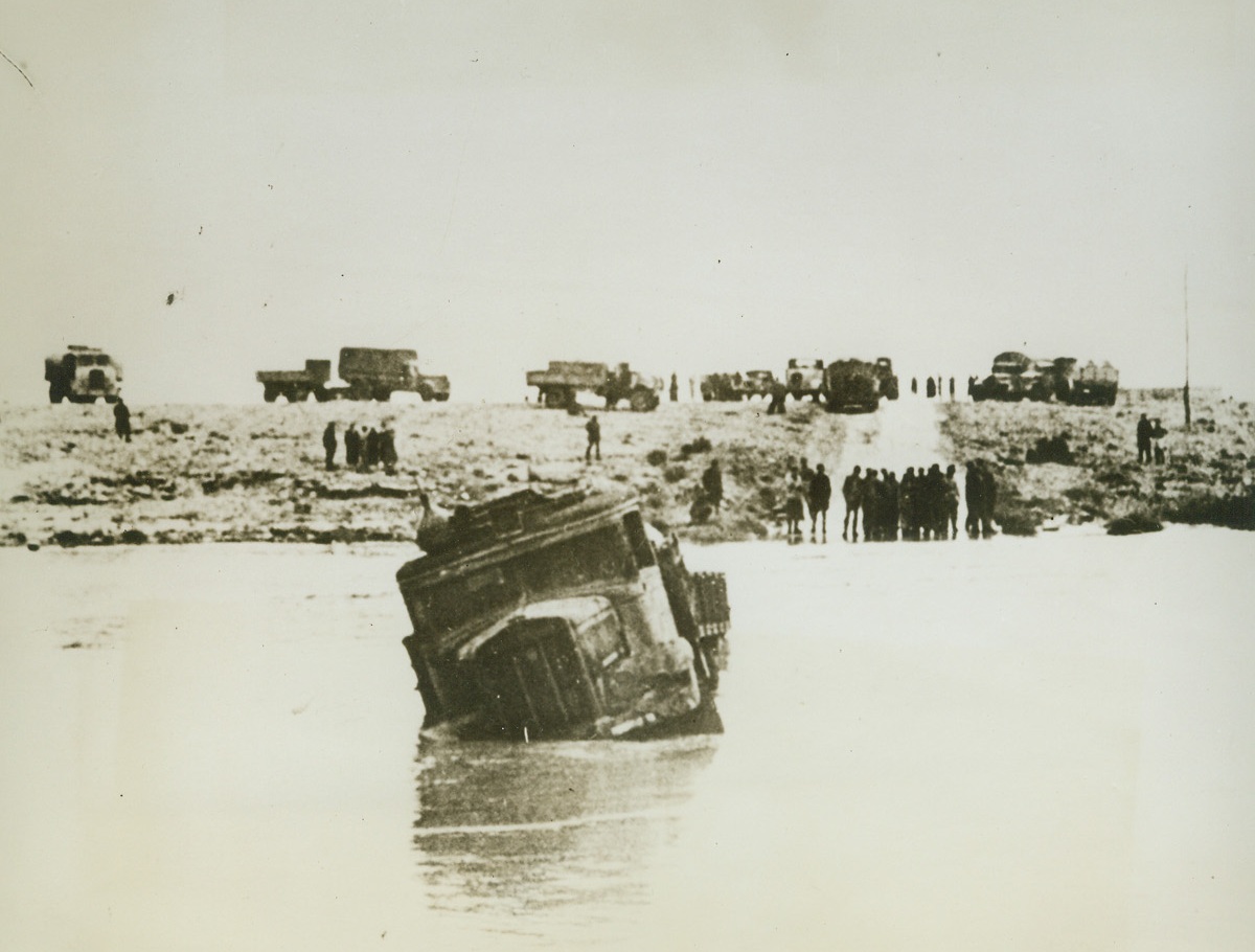 A German Column Bogs Down, 3/1/1943. According to the caption on this German photo, which has just been received in New York, by way of Lisbon, this motorized column of Nazi forces is shown halted along a road in North Africa as the result of one night’s heavy rain.  One truck, (foreground), is completely bogged down after unsuccessfully trying to plow through flood in foreground. Credit line (ACME);