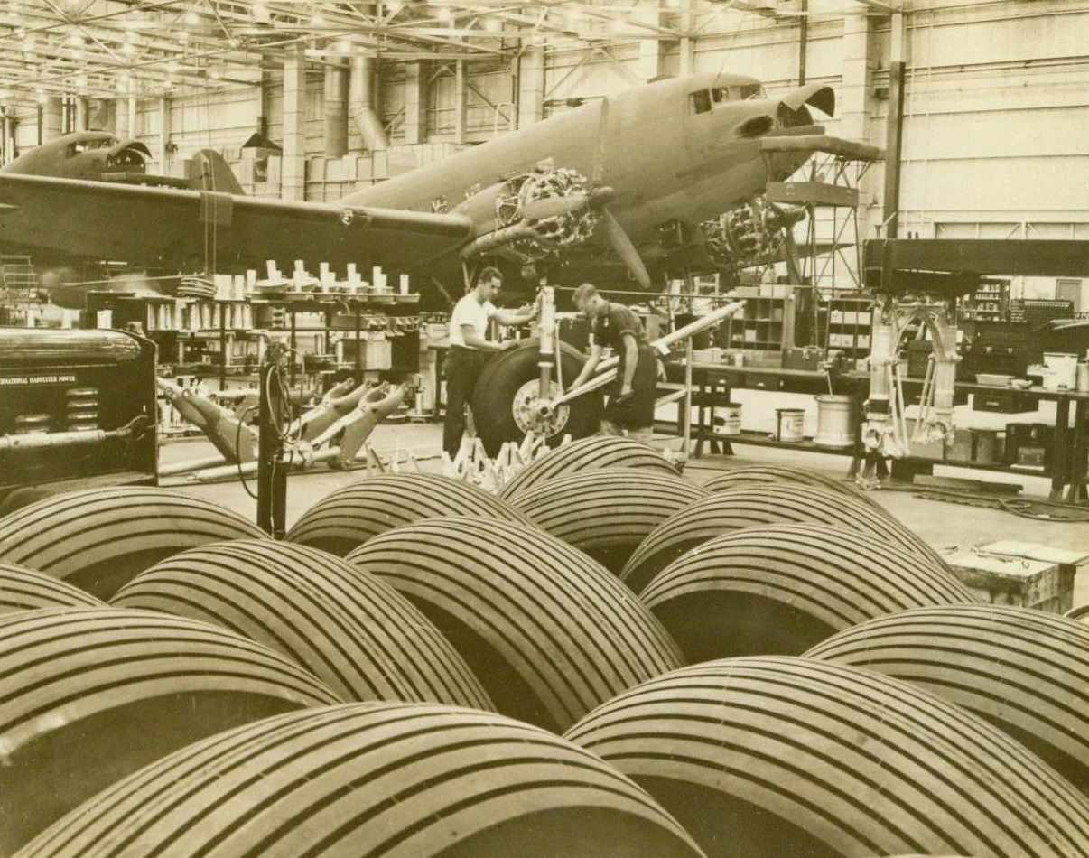 Round The Clock Birth Of American Air Power, 3/15/1943.  The awesome aircraft production figures of the United States come to life with a glimpse behind factory windows that are never dark. Out of steel, rubber, alloys and the sweat of man is created the American air might that is haunting the trio of Axis leaders. To do a round-the-clock job of crumbling the industries, supplies and morale of our enemies. Planes must be produced round-the-clock, rolling off production lines that operate with the efficiency of a single, well-oiled machine. Here are some cogs in that machine Here’s why, brother. These great hunks of rubber are casings for the landing wheels of the transport planes that are carrying fighters and supplies across oceans and mountain peaks. Civilians will get their tires—when the paratroopers come home to stay. 3/15/43 (ACME);