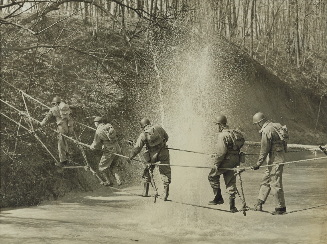 “Union Guests” Get Ranger Training, 3/23/1943. Camp Atterbury, Ind.: A group of CIO-UAW members that were invited to this camp, to find out how the Army lives, are shown as they crossed a rope bridge under actual war conditions as a bomb drops into the water nearby. The feat is part of the regular “Ranger” training, during which actual war conditions are copied. Credit: ACME.;