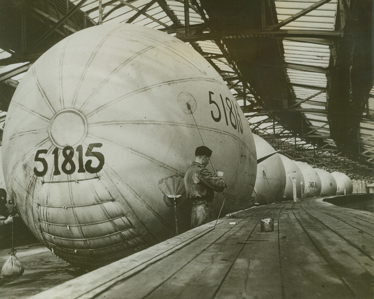 Inflation Line, 5/27/1943. SOMEWHERE IN ENGLAND—Mark VI balloons of the Royal Navy stand in line inside the inflation shed in which they are housed. Valuable because they help to protect ships from air attack, the balloons are used on drafters, trawlers, and other vessels.Credit: Acme;