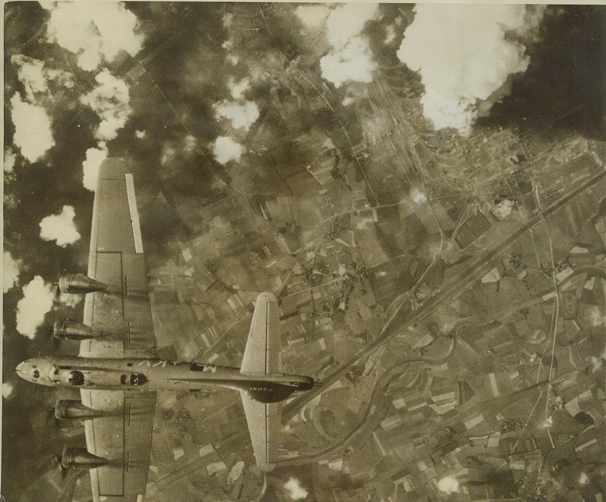 Rub-Out on Rubber, 6/29/1943. RUHR, GERMANY -- Hell breaks loose in the Ruhr, as a close-packed formation on Flying Fortresses scrambles synthetic rubber plants at Huls. The camera picked out this one Fortress out of the close formation flown by the big bombers to mass their fire power against enemy fighters. In the upper right hand corner the smoke from a blasted factory rises up over the target area as group after group of Fortresses roar through their bombing runs. Credit: (ACME);