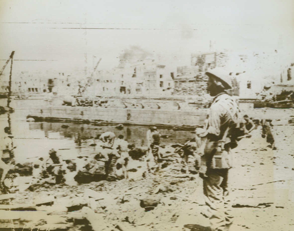 Italian Prisoners Bathe After Capture, 6/14/1943. PANTELLERIA – The above photo, flashed here by US Army Radiotelephoto, shows Italian prisoners who were captured on Pantelleria washing in the harbor supervised by a guard in the foreground. In the background may be seen the ruins of the island with some areas still smoking.  Credit (British Official Photo from Acme via Radiotelephoto);