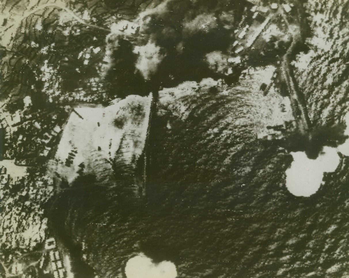 TAKING ITS DAILY BEATING, 6/7/1943. PANTELLERIA—The island stepping stone from Runisia to Sicily gets a terrific pounding from Allied sea and air forces daily in the pre-invasion softening up process. Smoke rising at top of photo is from burning oil dump in the harbor. Oil storage tanks and barracks were damaged in the latest attack. Credit: Acme radiophoto;