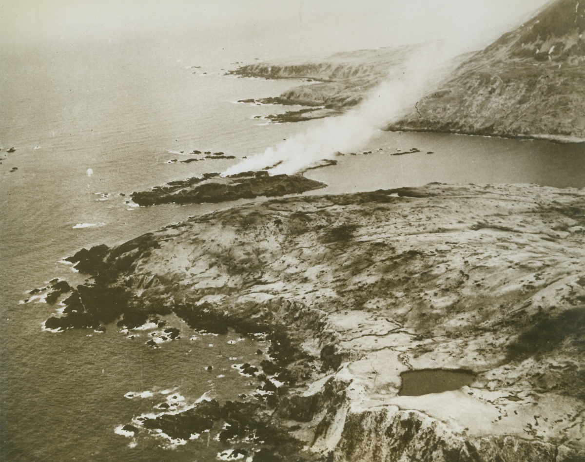 JAPS’ LAST STAND, 6/16/1943. Smoke rises from fires started by American air and ground forces on the small island of Kinnaw, off Chicagof Harbor, Attu, where the Japanese made their last stand. A U.S. Navy plane few over the shell and bomb pocked hills to make this photo on May 31st. Credit: Official U.S. Navy photo from Acme;
