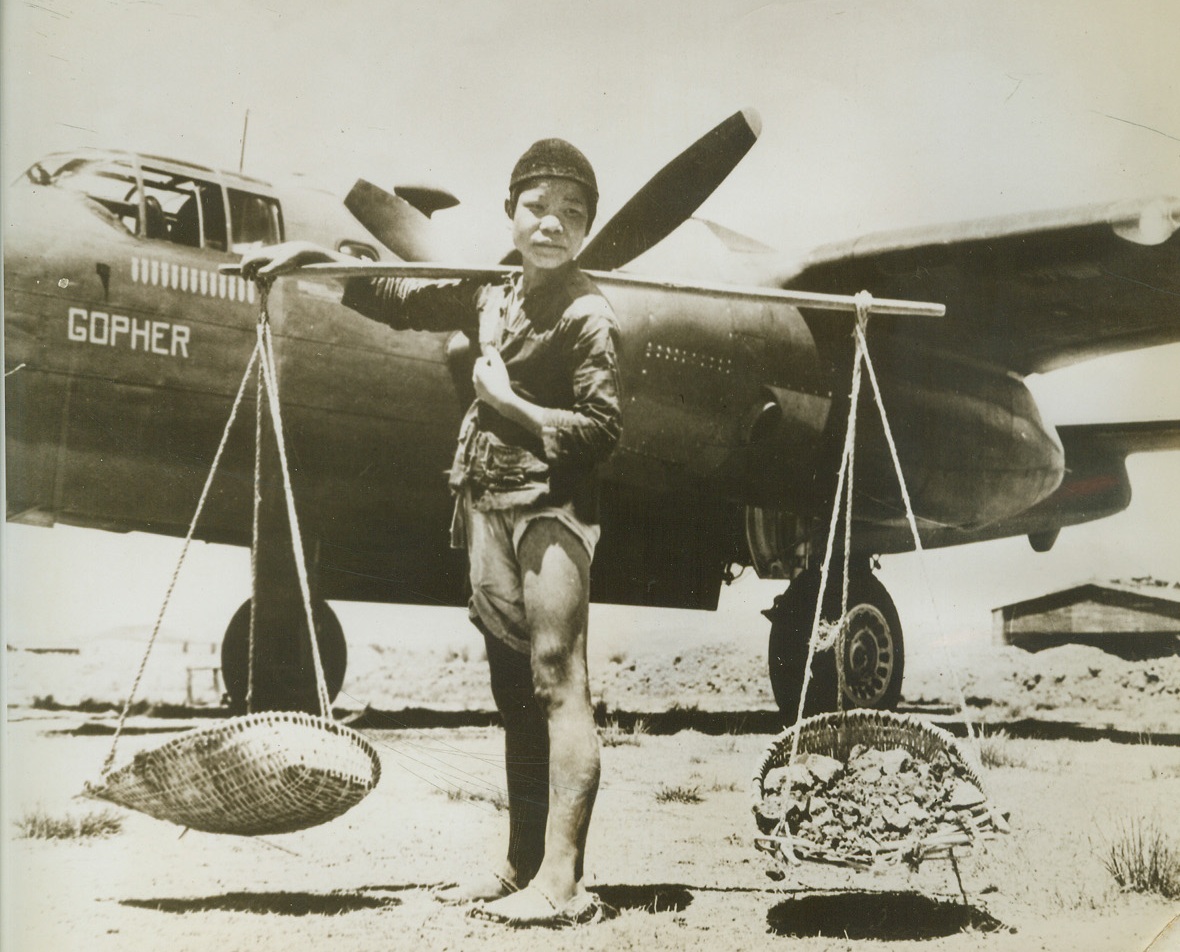 CHINESE BOY HELPS BUILD AIRFIELD, 6/26/1943. SOMEWHERE IN CHINA—This young Chinese lad pauses in front of an American B-25 as he carts hand-crushed stones to be put into place on an airfield that is being built by Chinese men, women and children. Several underlayers of the crushed stone go into the building of the field and it is surprising how quickly the job can be done by using these simple methods.Credit: OWI PHOTO FROM ACME.;