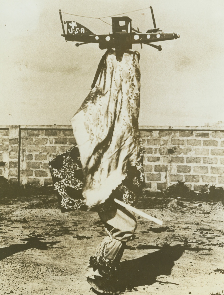 White Man’s Ju-Ju, 6/1/1943. North Africa – A modern witch doctor in North Africa replaces his traditional mask with a model US airplane, the B-40, which he built complete with antenna and U.S. Star Bushmen call the plane the “steam chicken.”  For hundreds of years the medicine men held to tribal masks passed down from generation to generation.  Now, supplanting the traditional mask with the stronger Ju-Ju of the white man the medicine men descend on tribes in flying echelon as the evil sprits of the Nazis are driven out of Black Men’s territory.Credit line (Official photo from ACME);