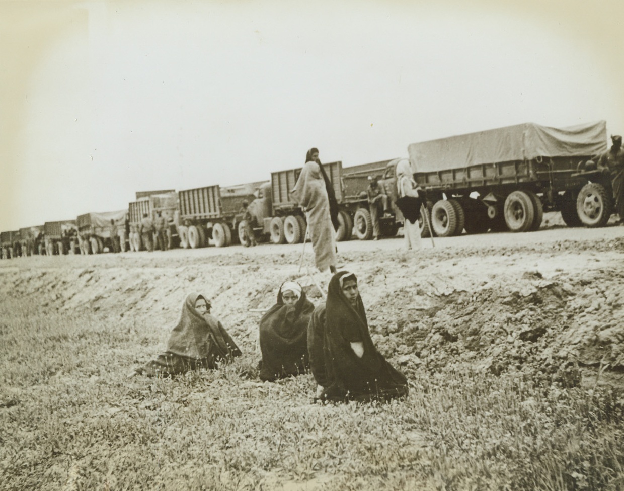 Heading for Russia, 6/4/1943. Native Iranian boys turn away from a long convoy of supplies enroute to Russia just long enough to have their pictures snapped. The United States truck train is making a rest stop somewhere in the Persian Corridor, and the sight thrills the natives. Credit: ACME.;