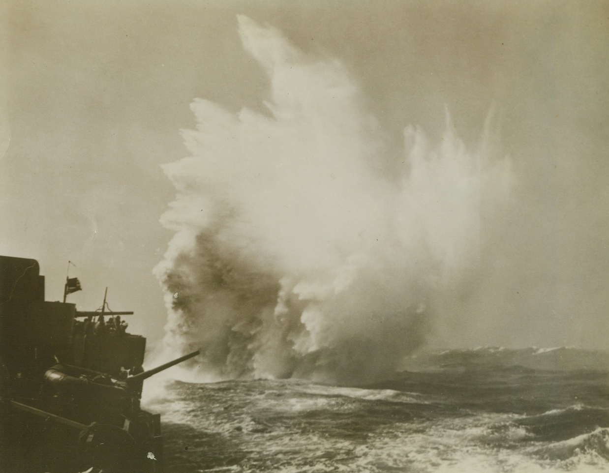 Depth Charge Chases Sub, 6/10/1943. Somewhere in the North Atlantic—A foaming geyser shoots skyward alongside an unidentified American destroyer (left) as a depth charge is sent down to chase an Axis sub away from an Africa-bound convoy. Escorting millions of tons of supplies for fighting men, battling destroyers kept losses under 2%, according to an official Navy report. Credit: Official U.S. Navy photo from ACME.;