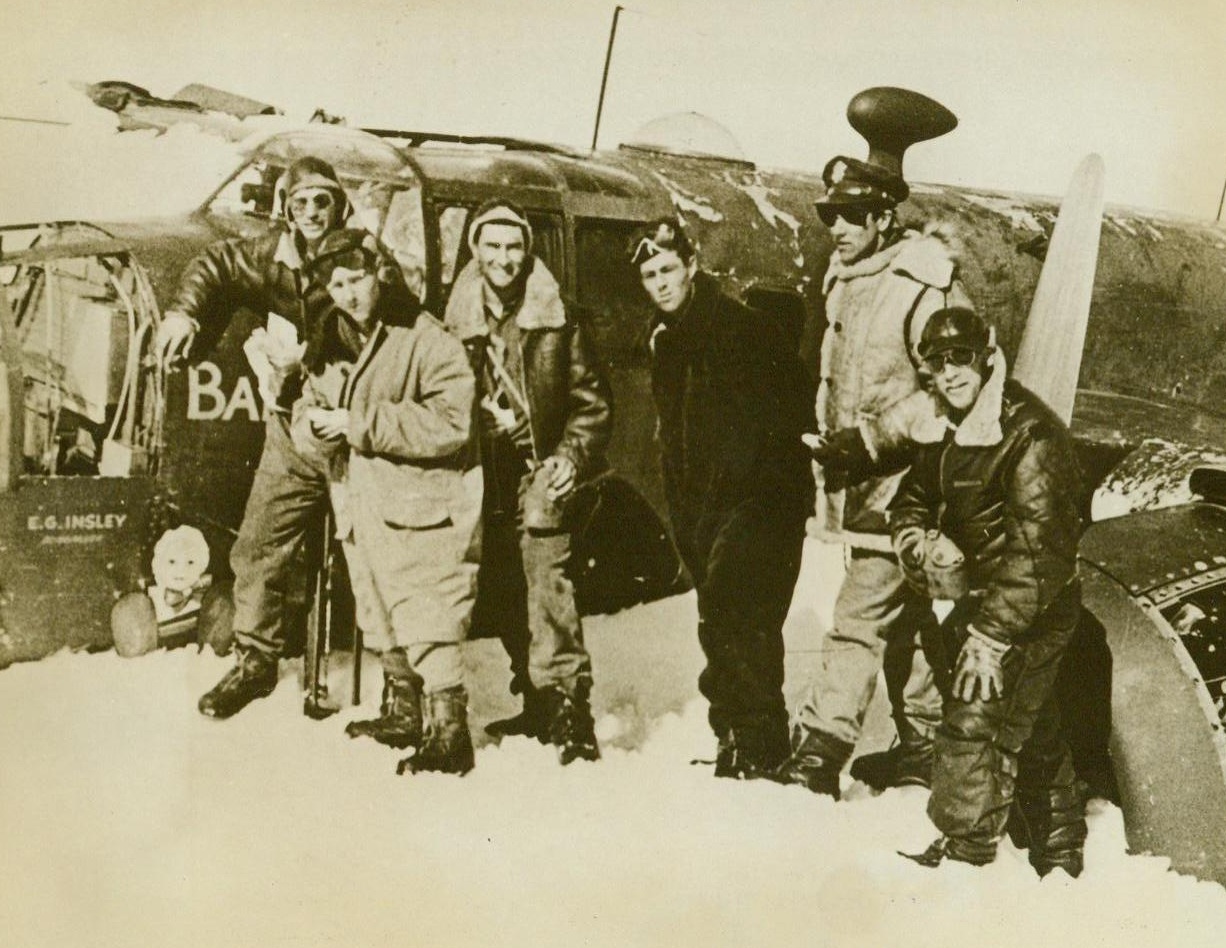 Fliers Rescued After Crash, 6/28/1943. Greenland – Crewmembers and their Mitchell B-25 Patrol Bomber are shown after their ship crashed on the coast of Greenland, when it ran out of fuel on a patrol flight through bad weather. They lived for four days on emergency rations and water melted from snow. Their weak radio signals brought a plane, and then a Coast Guard vessel, which rescued them. Left to right, are: Sgt. J. Whitehead, Engineer; Sgt. J.R. Brewster, Radio Operator; Sgt. C.C. Cook, Operator; Lt. J.I. Moor, Co-Pilot; Lt. J.J. Blais, Pilot; and Sgt. J.C. Whitman, Bombadier. 6/28/43 (ACME);