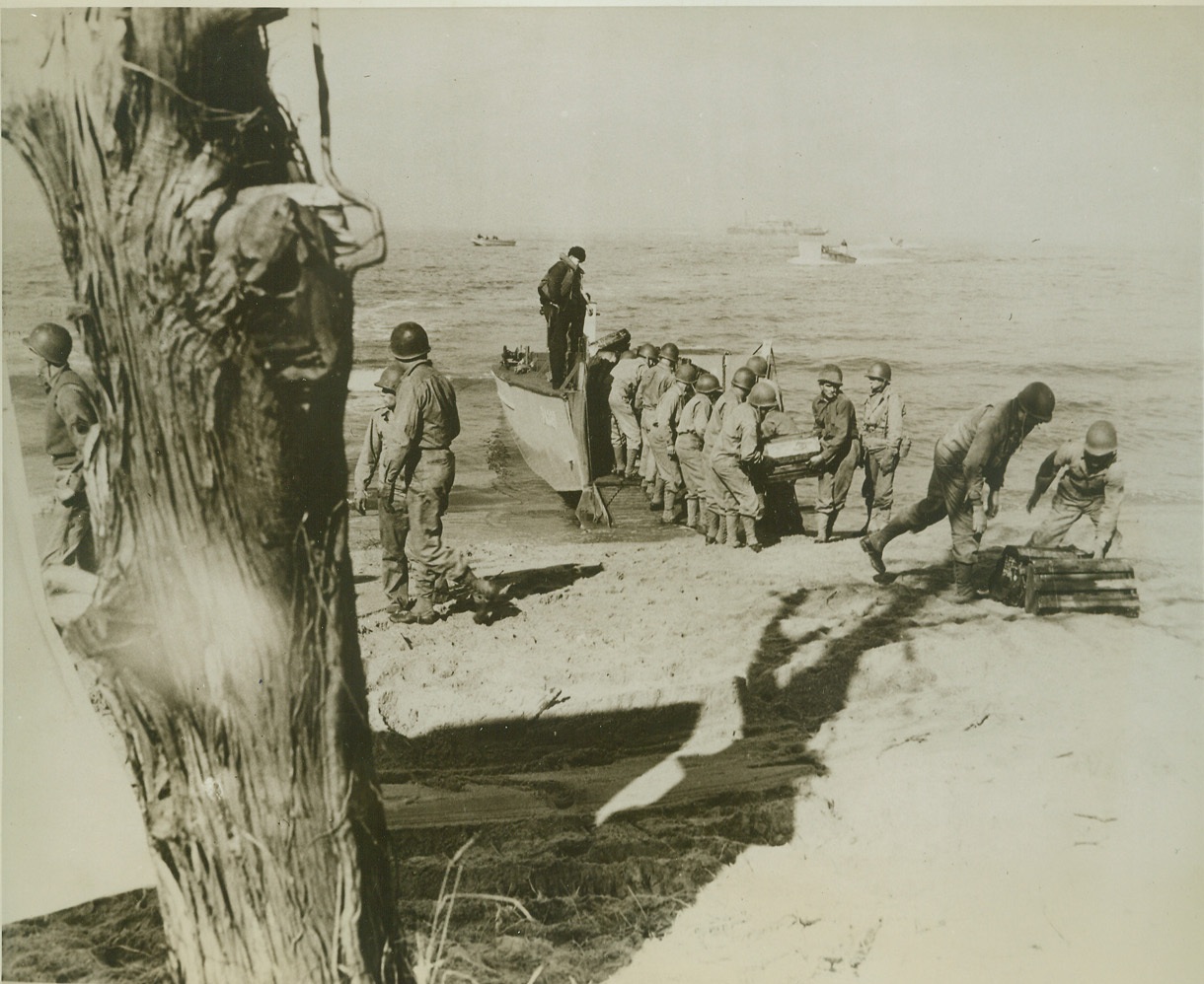 Bringing Up the Ammunition, 6/17/1943. Somewhere on the East Coast—Carting heavy loads of ammunition from a landing barge, these Yanks hold a dress rehearsal in preparation for the day when they’ll stream from U.S. Navy transports to invade enemy seaside strongholds, training to work as part of a unified Army-Navy amphibious force, composed of ricked officers and men from both services, these boys learn to carry out the most difficult of all military assignments—landing on a fortified, hostile shore. Credit: Official U.S. Navy photo from ACME.;