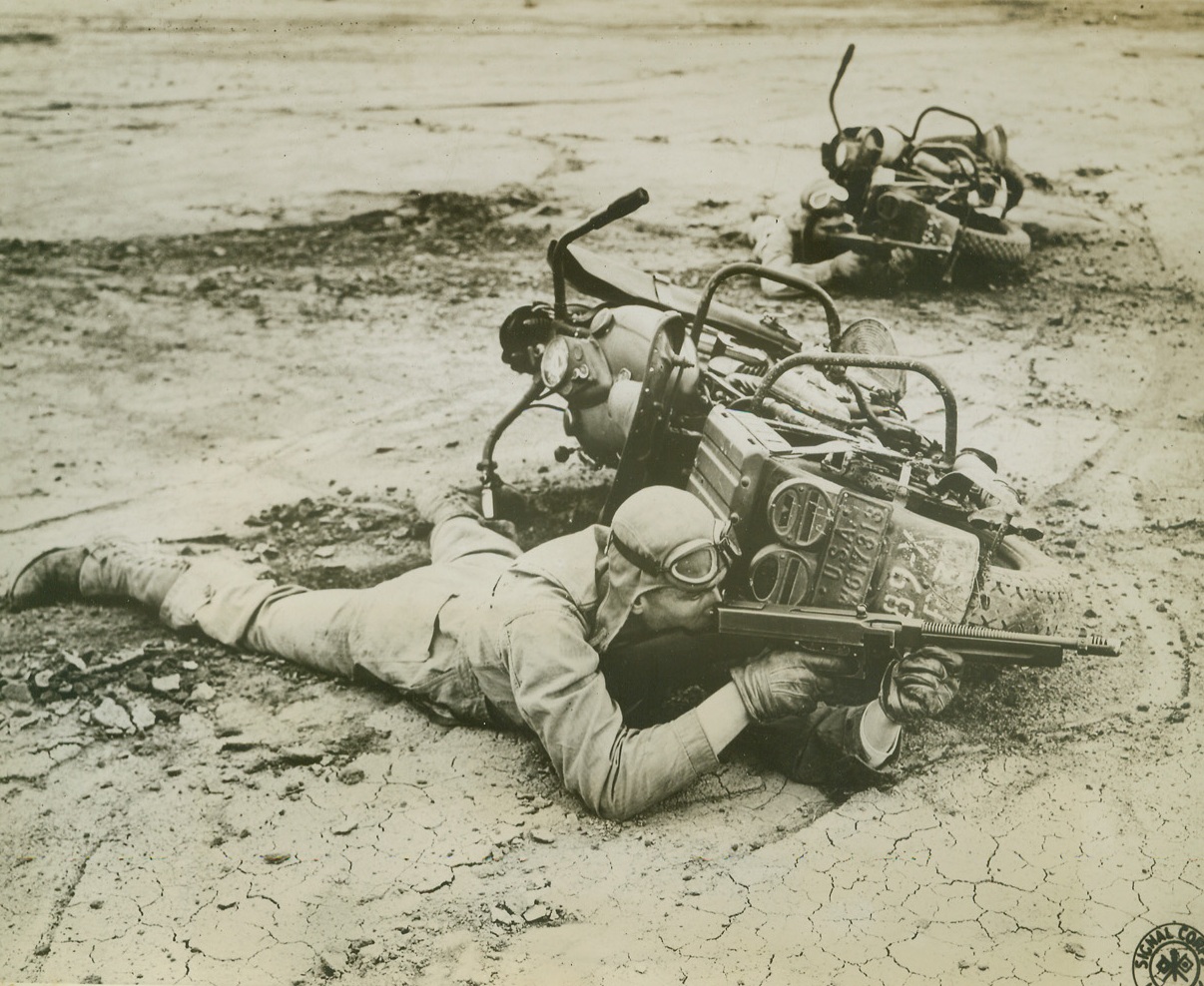 ROUGH WORK BUT THEY LIKE IT!, 8/23/1943. CAMP CARSON, COLO.—Commando training has nothing on the work these rough riding cyclists of the Reconnaissance Troop, Camp Carson, Colo., do to keep themselves and their machines ready for the battle front where paved highways are apt to be conspicuous by their absence. A soldier’s motorcycle makes a good shield in combat.Credit: U.S. Signal corps from Acme;