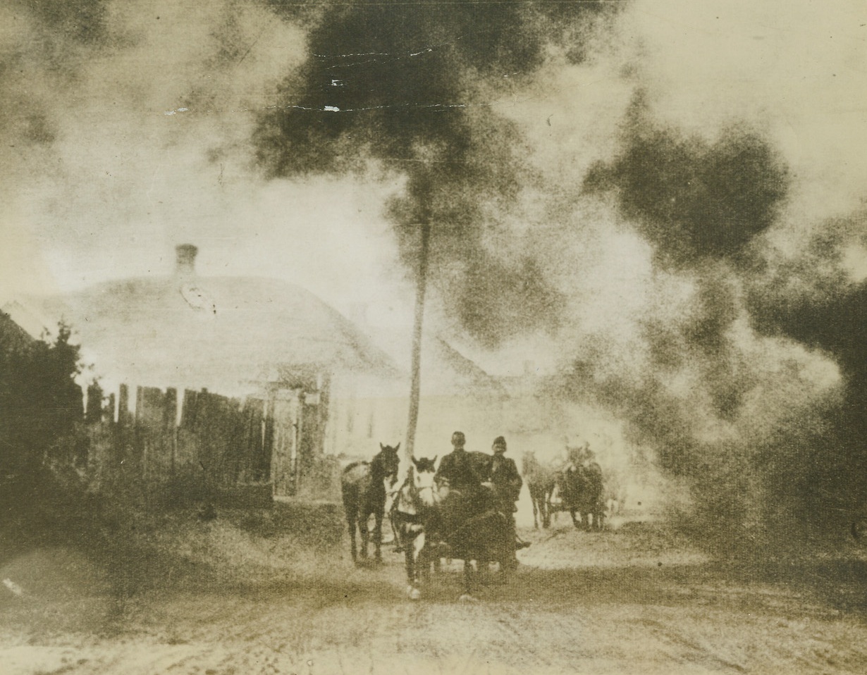 Retreating Through Fire, 8/30/1943. Russia—Through a trail of death and destruction of their own making, German reserves, in horse-drawn carts, move up to the front line on the Dnieper Bend. They pass through a small Russian village, set afire by some of the retreating Nazis before them. Photo has just been received from London, obtained through a neutral source. Credit: ACME;
