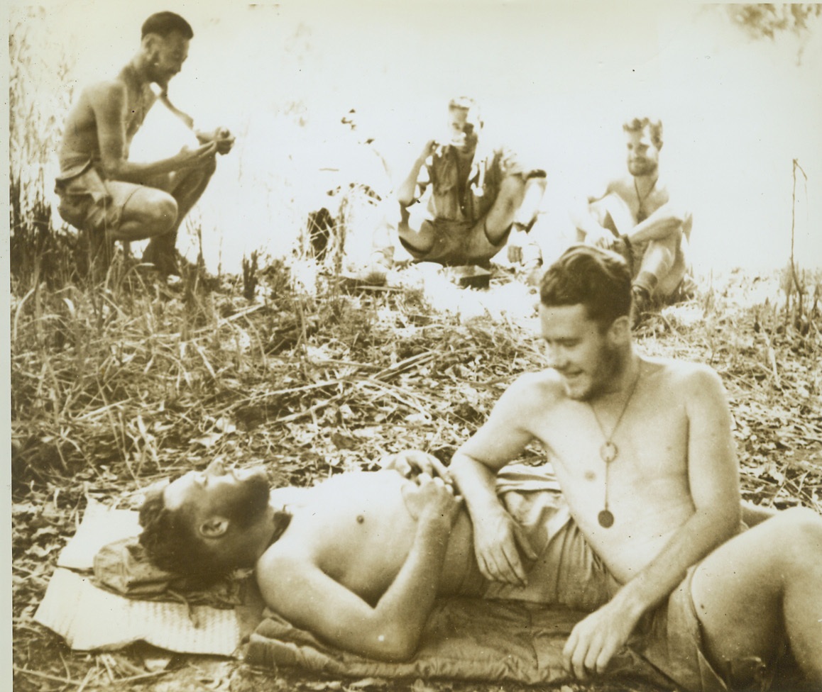 TIME OUT FROM SNIPING, 1/25/1943. TIMOR ISLAND – Australian guerillas rest in their jungle hideout on the Jap-held island of Timor. These Aussie snipers live virtually in the midst of the enemy and are as annoying to the Nips as a deluge of red ants. (Passed by censors.) Credit: ACME;