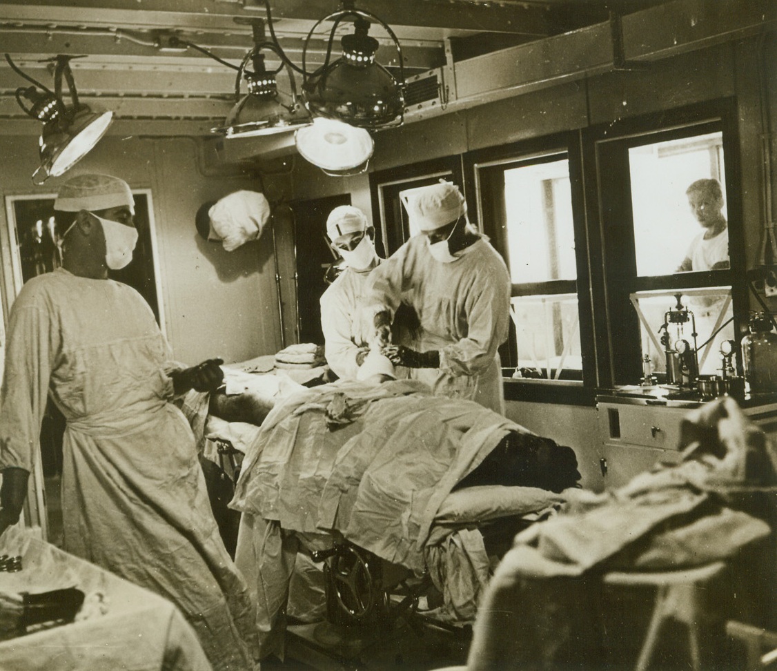 HAPPY PATIENT, 1/1/1943. ABOARD THE U.S.S. SOLACE—This patient doesn’t seem to mind it a bit as the doctor puts a cast on his fractured leg. Equipment aboard the Solace, navy hospital ship, is as complete as in any hospital in the U.S. It is a converted passenger liner that used to run from New York to Miami. Now it travels alone, unarmed, with no passengers, and only guns aboard are a few 45’s for internal protection. It is the only ship in the Navy painted white with a green band around the sides and a red cross on either side and on the smoke stack.Credit: Acme;