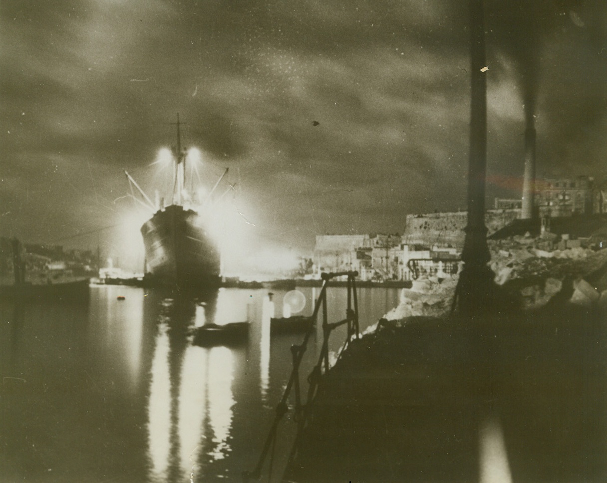 United Nations Convoy Reaches Malta, 1/12/1943. MALTA – A battery of arc lights illuminates the unloading by night of a British convoy at Malta. Ashore, the population of the battered island celebrate the landing of several months’ supplies. By winning back Libyan air bases, the British have been able to protect a series of convoys, some of which reached Malta unmolested. All arrived unscathed. Credit Line (Acme);