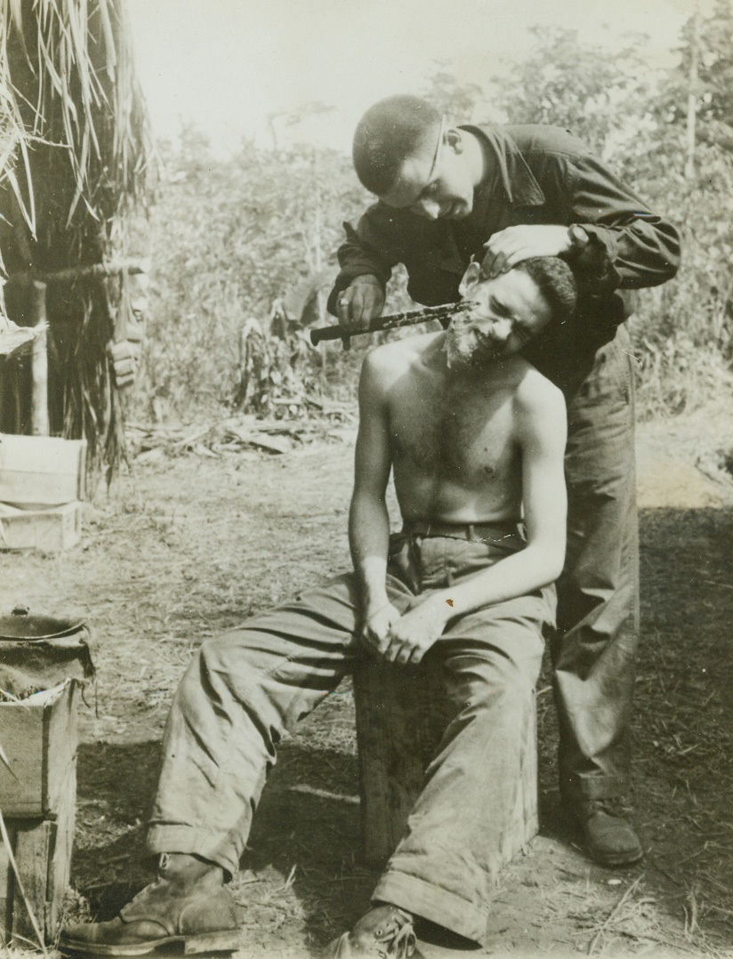 Close Shave, 1/13/1943. New Guinea: Lt. Harold Evans, of Robersonville, N. Car., keeps his bayonet razor sharp, so Lt. Henry Gibbs, of Morehead City, N. Car., felt just like he was getting a shave from a home-town barber. Both boys are seeing plenty of action on the Buna Front. (Passed by Censor) Credit: ACME;