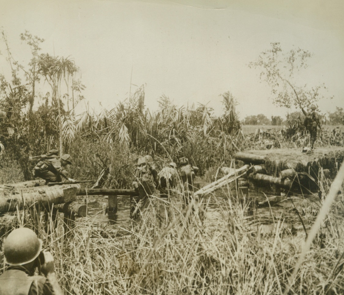 Yanks Move Forward, 1/13/1943. New Guinea: - Just ten minutes before this picture was taken, Japanese forces covered this wooden bridge over Simemi creek with baking machine gun and artillery fire from the right bank.  The attack by the American forces pushed the Japs back, and here you see the Yanks scrambling across the remains of the bridge.  It was one phase of the attack to take Simemi creek on the Buna front. Credit line (ACME);