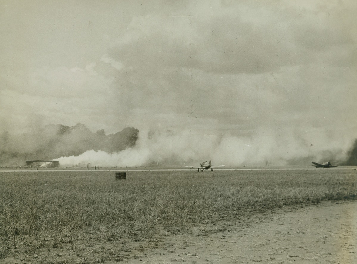 Japs Make Direct Hit, 1/16/1943. Guadalcanal, S.I. – Clouds of white smoke pour from a hangar at Henderson field on Guadalcanal during a Jap raid, marking the spot where enemy bombs found their target.  It was a direct hit.  The two planes shown in photo apparently escaped the attack. Credit line (Official Marine Corps photo – ACME);