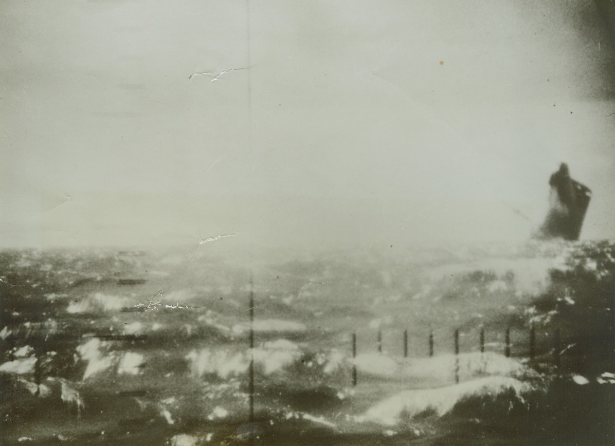 American Submarines Attack Jap Shipping, 1/23/1943. This picture made by an alert Navy cameraman from the periscope of the attacking American submarine.  In a rising crescendo of death and destruction, three torpedoes crash into this unsuspecting Japanese merchantman, of more than 9,000 gross tons.  Lying in an unidentified Pacific harbor.  Heavy smoke rolls up from the stricken vessel has already concealed all but the camouflaged bow from the photographer in the submarine, who took the picture thru the periscope. Credit line (U S Navy official photo from ACME);