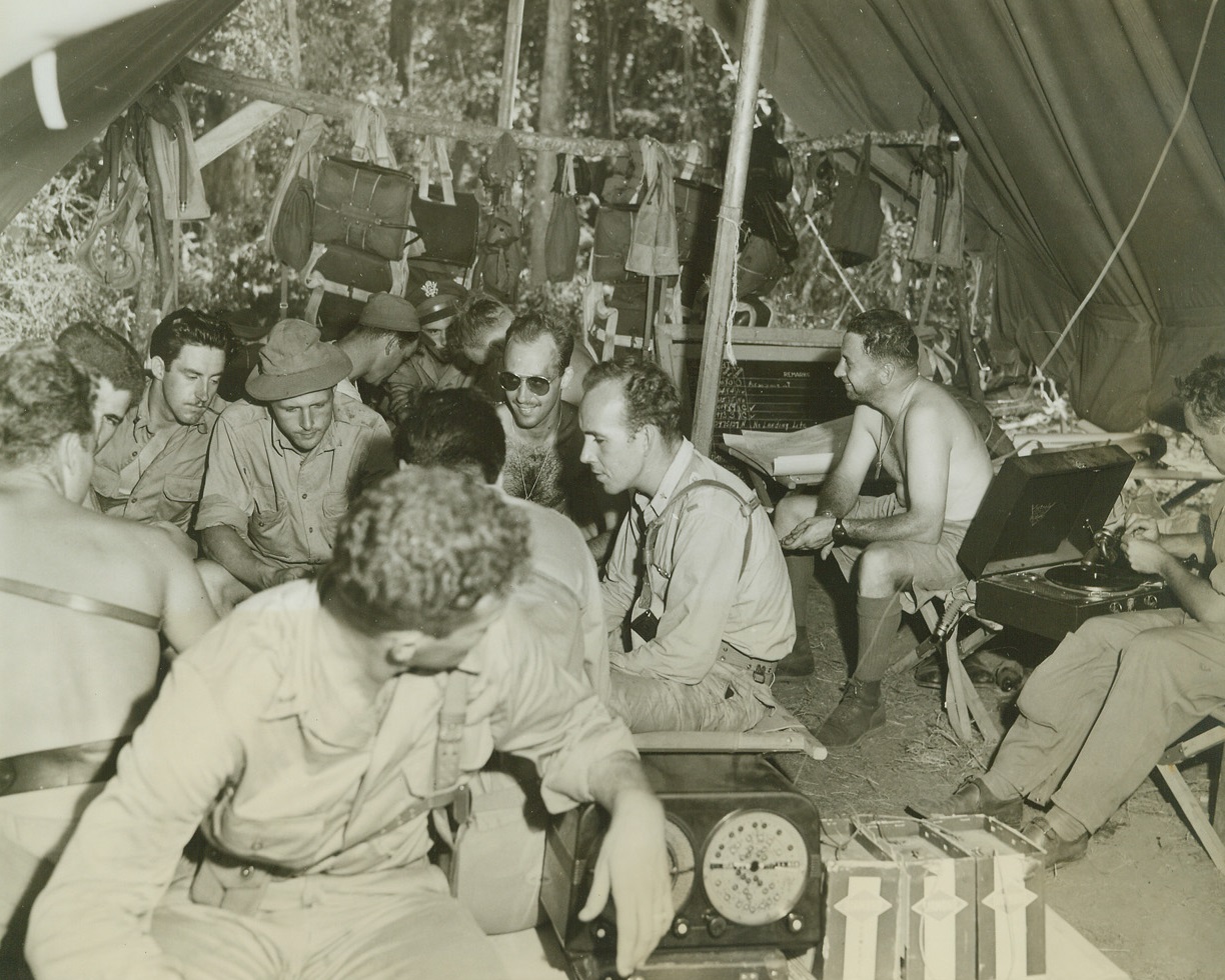 Awaiting the Call, 1/10/1943. Port Moresby, New Guinea – A new fighter group with their speedy P-38’s are now on the job at Port Moresby.  The boys have been on the alert ever since their arrival.  Here a group of American fighter pilots for the P-38’s play cards, listen to records and radio, or just sit as they await the call to go into action.  Note the chutes hanging in the rear of the tent. Credit line (ACME);