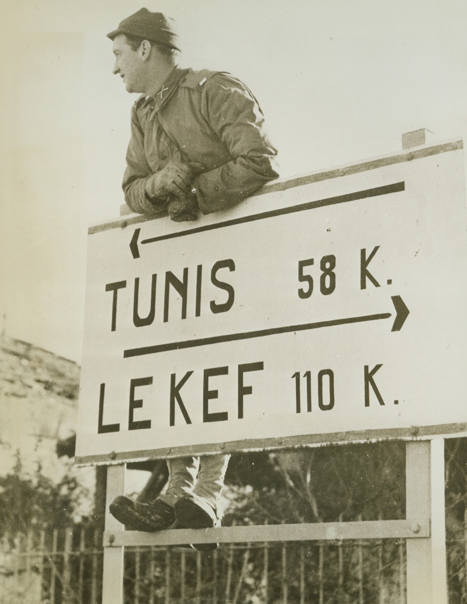 This Way to Tunis, 1/6/1943. Tunisia – This American soldier knows where he’s going – but he’s taking time out to get his wind before heading for Tunis, only 58 kilometers away.  Latest reports from that area indicate that the allies are closer to the key city than that.  A lightening British Commando-led attack is reported to have wrested the heights of Jebel Azzeg from the Nazis. Credit line is not visible.;