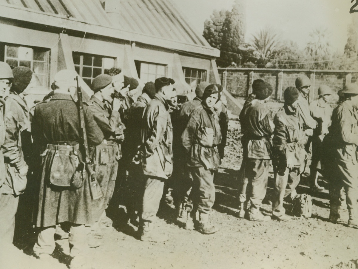 Our Boys --- Prisoners, 1/9/1943. Somewhere in Tunisia – A group of American and British prisoners wait, under guard, to be taken back to rear positions.  They were captured during fighting in Tunisia.  Photo was received through neutral sources in Portugal.  Latest reports indicate that the Nazi’s are shifting command on the Tunisian front, and that Major General Walther Nehring has bee superseded by General Von Arnim as Commander-in-Chief of axis forces there. Credit line (ACME);