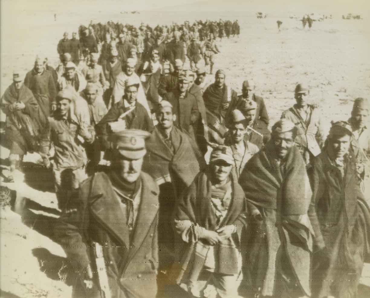 Nazi Prisoners Near Tripoli, 1/25/1943. North Africa—Italians and Germans who were captured near Tripoli are shown being marched back to a waiting transport. Note that the prisoners have been carefully separated, with the Italians in front and the Germans behind. Photo radioed from Cairo at noon today.Credit: ACME radiophoto.;