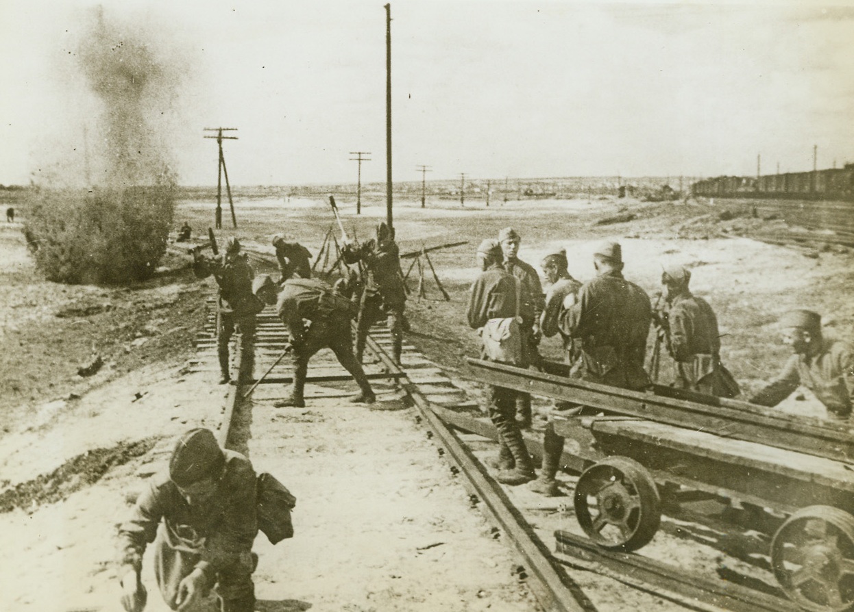 Red “Track Team” Under Fire, 1/26/1943. Southwestern Front—Although under heavy shell fire from the enemy, these Russian engineers repair and re-lay the track of a railway line in territory recently recaptured from the Nazis. It’s a tough job for these soldiers, for they often break through German lines to rip up rail lines in the enemy rear areas to cut off their retreat. Then, when the Russians have captured this territory, the lines must be repaired. (Passed by censors). Credit: ACME.;