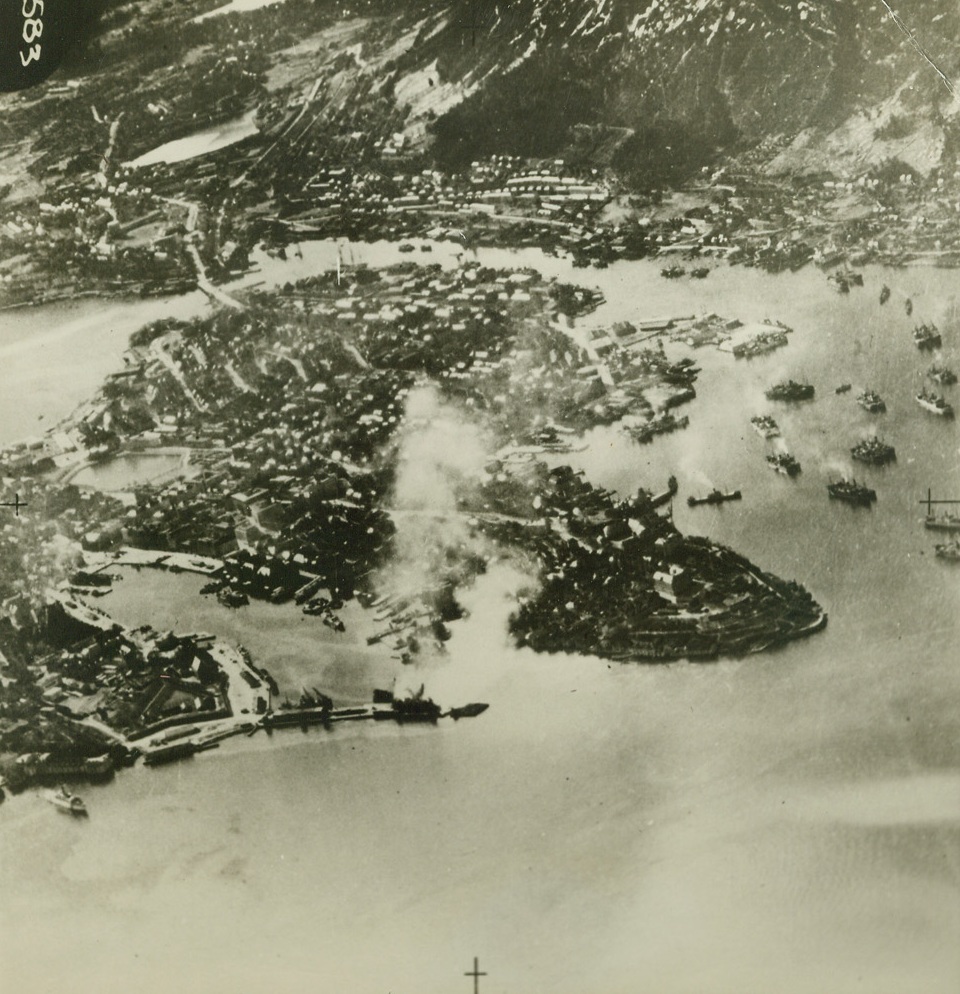 RAF Over Bergen Harbor, 1/13/1943. London, England – Photo was made by planes of the RAF coastal command, flying over Bergen Harbor during an RAF attack. The harbor is crowded with German transports and supply ships, one of which is burning at the quayside after the attack. Photo will soon be published in a book, showing the value of photographic reconnaissance work by the RAF coastal command, in the destruction of enemy equipment by the United Nations. Passed by censors. Credit: ACME;