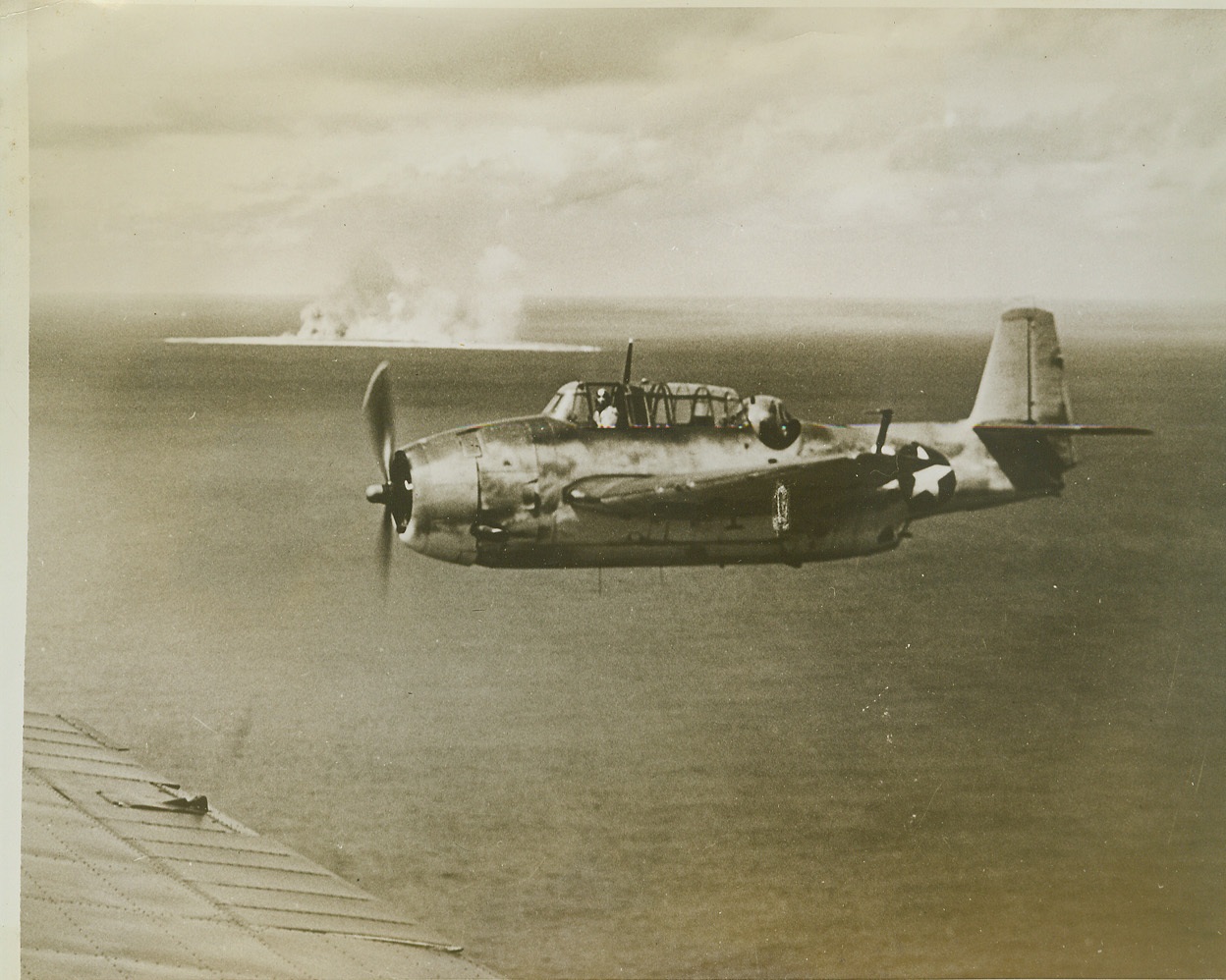 Navy Blasts Marcus Island, 9/28/1943. Smoke from burning Japanese installations covers tiny Marcus Island as a Grumman Avenger torpedo bomber, which has just dropped its load on the enemy base, returns to its carrier. The Japanese island base, 990 miles southeast of Tokyo, was attacked by a U.S. Navy task force on September 1, 1943, and 80% of the enemy installations were reported destroyed. Credit: (U.S. Navy Official Photo from ACME);