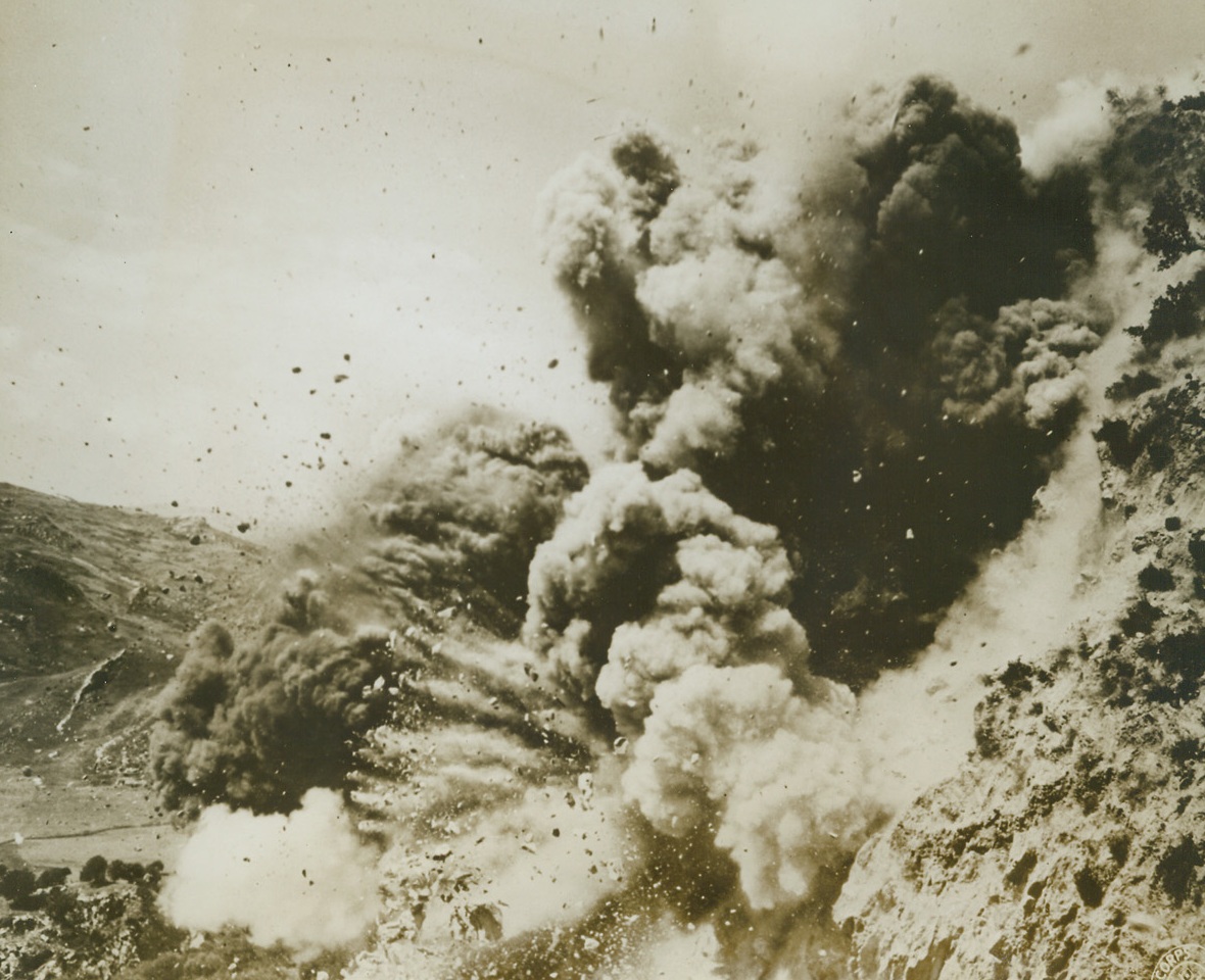 THE BIG BANG, 9/24/1943. SICILY—Clumps of sod mix with clouds of smoke and dust as demolition charges of American combat engineers do their stuff in Sicily. The charges were used to clear a series of road blocks built by retreating Axis fighters. Credit: Signal Corps photo released through Treasury War Bond Drive—from Acme;