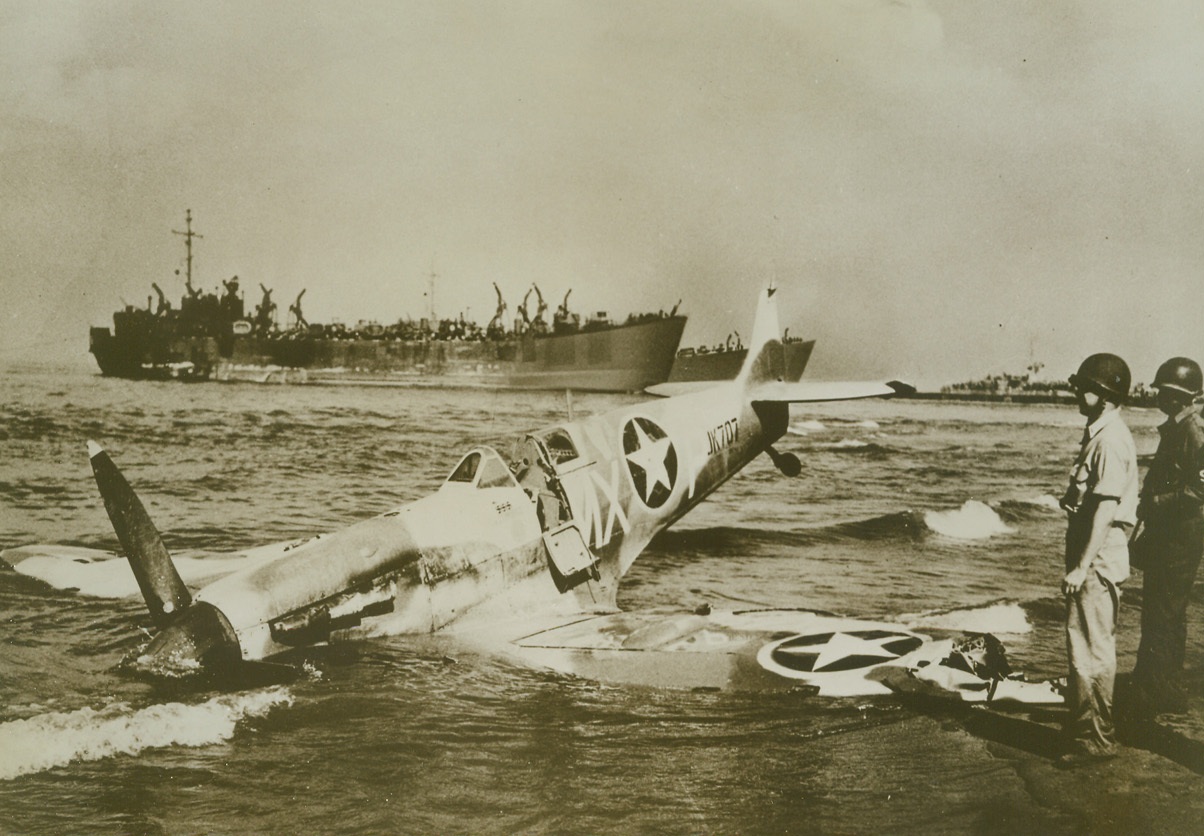 Forced Landing, 9/23/1943. PAESTUM, ITALY – This Spitfire fighter, bearing the insignia of the U.S. Army Air Forces, was forced into a crash landing in the surf at Paestum during bitter fighting in that area. Note three Swastikas painted on side of cockpit (just under windshield). At the right, a U.S. Army Lieutenant and a U.S. sailor of the shore Patrol, examine the ship. In background, can be seen landing craft and transports manned by U.S. Coast Guardsmen. Credit Line (U.S. Coast Guard Photo from Acme);
