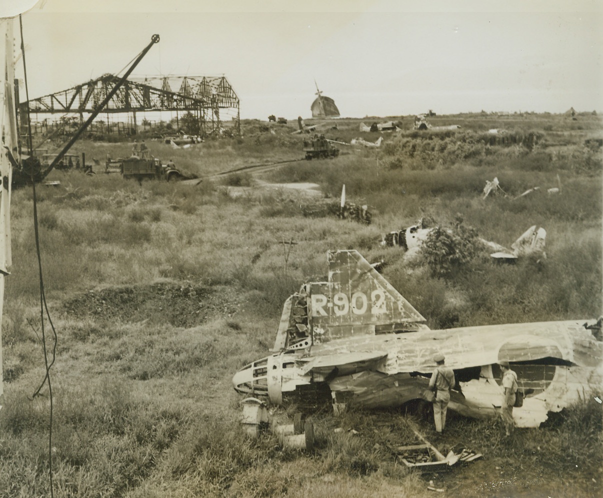 Littered Airfield, 9/30/1943. Lae, New Guinea – Wrecked Japanese Warbirds and debris from a bomb-ruined hangar litter the captured airfield at Lae. In the background, a half-sunk enemy ship tilts at an angle. Latest reports from New Guinea indicate that Australian forces have advanced deeper into Jap defenses around Finschhafen, while Allied fliers continue to pound the air base at Wewak 9/30/43 Credit Line (Photo By Frank Prist, Jr., ACME Photographer For War Pool);